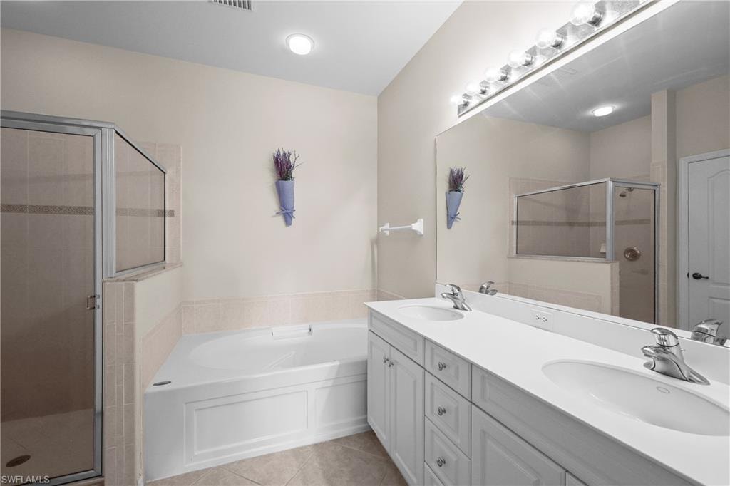Primary Bathroom with a garden tub, light tile patterned floors, a stall shower, and double vanity