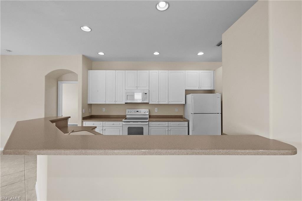 Kitchen featuring white appliances, recessed lighting, white cabinets, light tile patterned flooring, and a kitchen bar
