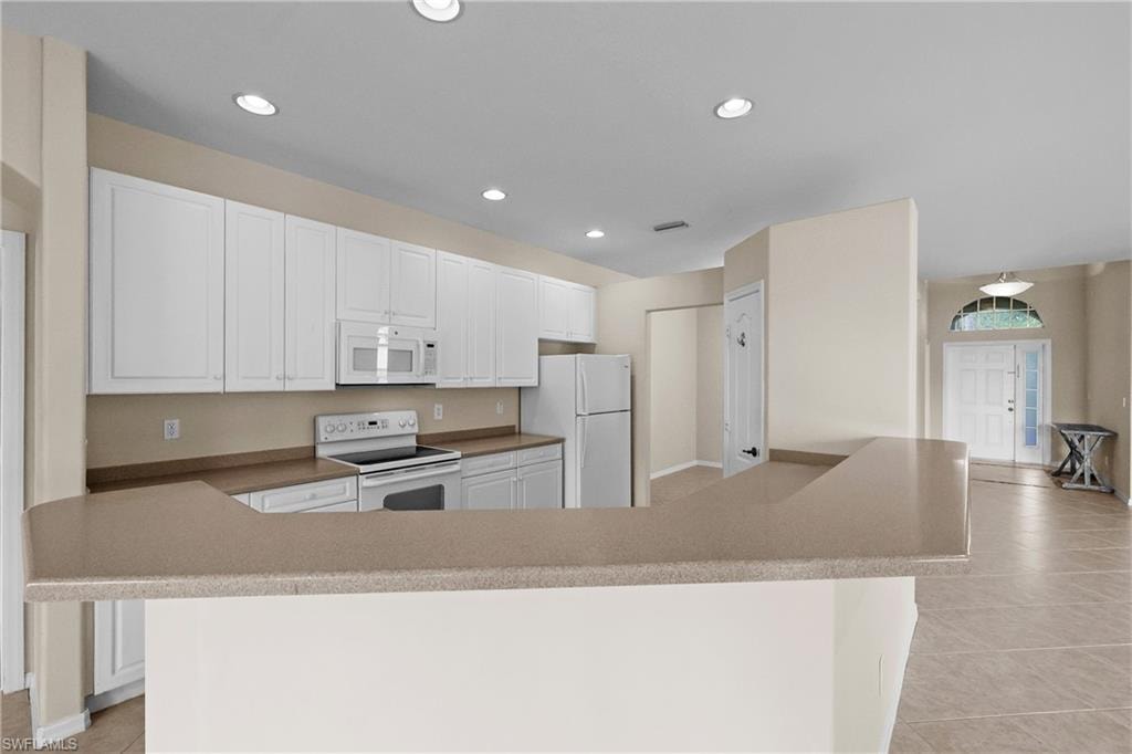 Kitchen with light tile patterned flooring, white cabinetry, white appliances, large pantry and recessed lighting