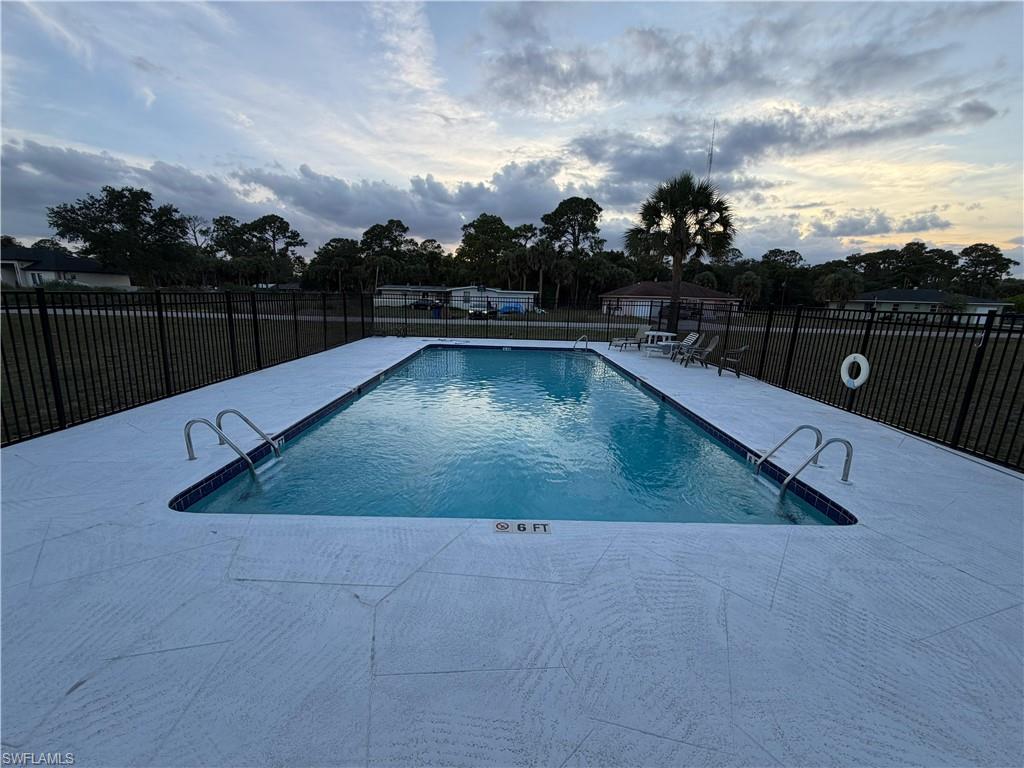 Rectangular swimming pool with white textured decking and a black metal fence