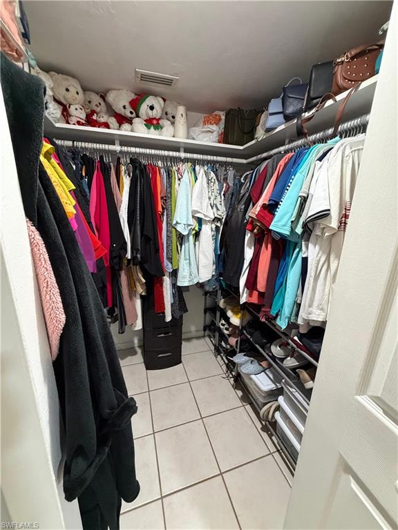 Walk-in closet featuring extensive built-in shelving, multiple hanging rods, and light-toned tile flooring