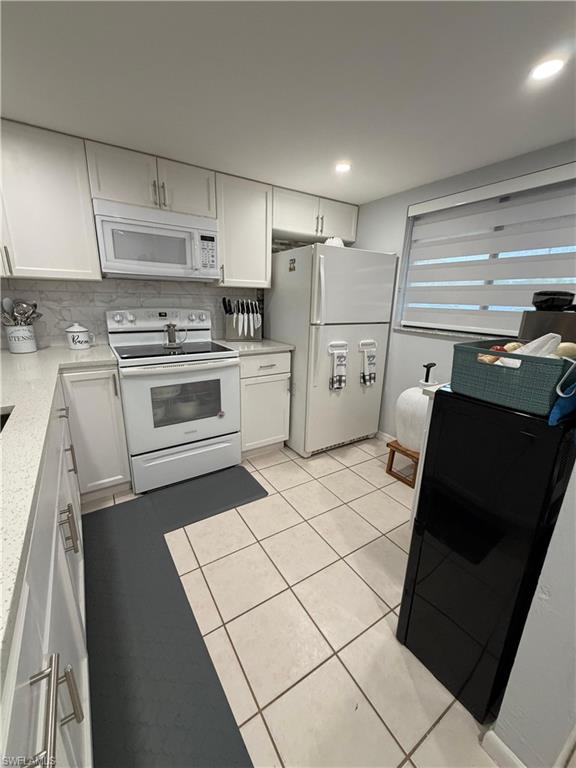 Kitchen featuring light-toned cabinetry with brushed nickel hardware, white appliances, and a mosaic tile backsplash