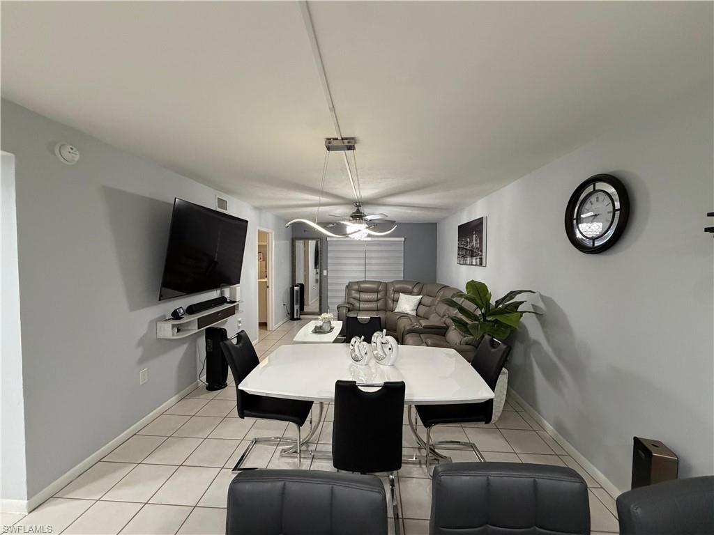 Open-concept living area featuring light-toned tile flooring, a wall-mounted media console, and a contemporary ceiling fan with integrated lighting