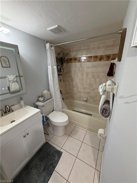 Bathroom featuring a tile-surround bathtub, white vanity with integrated sink, brushed nickel faucet, and square tile flooring