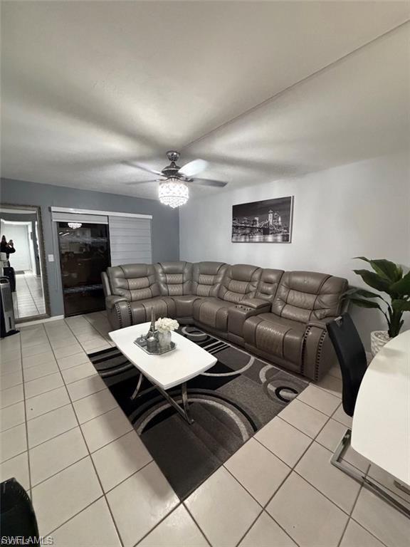 Living area featuring neutral-toned tile flooring, a ceiling fan with a decorative light fixture, and a sliding glass door