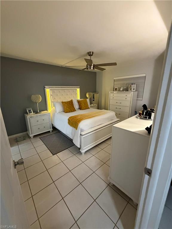 Spacious bedroom featuring light-colored tile flooring, a dark accent wall, and a ceiling fan with integrated lighting