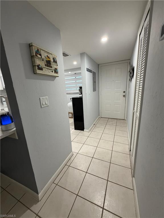 Entry corridor featuring square tile flooring, a paneled entry door, recessed ceiling lighting, and louvered bifold closet doors