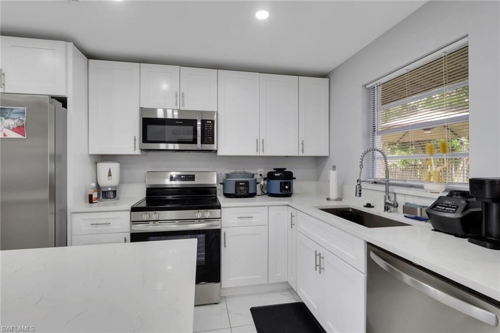 Modern kitchen featuring white cabinetry, stainless steel appliances, light-toned countertops, and a window with horizontal blinds