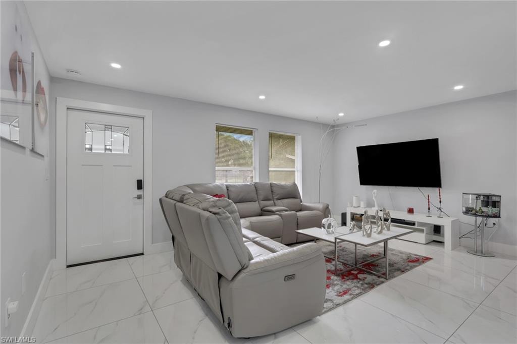 Bright living area featuring white tile flooring, recessed lighting, white walls, a white entry door with decorative glass inserts, and two windows providing natural illumination
