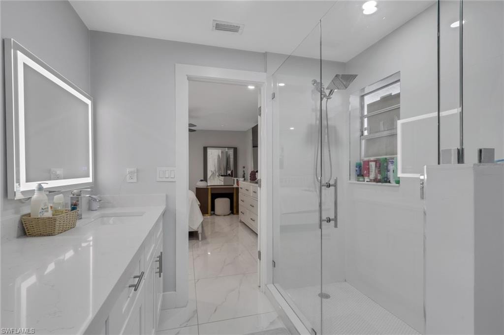 Bathroom featuring a glass-enclosed shower with a rainfall showerhead, a window with horizontal blinds, and a vanity with a quartz countertop and an illuminated mirror
