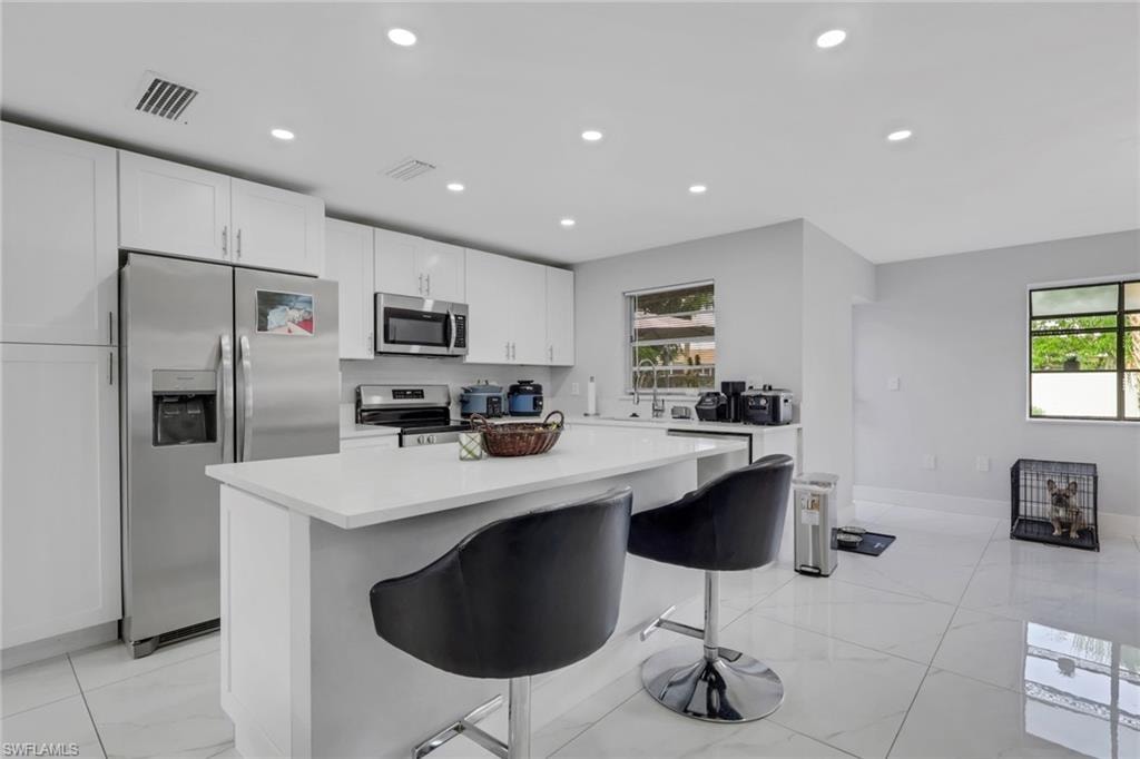 Contemporary kitchen featuring an island with seating, white shaker cabinetry, stainless steel appliances, and large format tile flooring