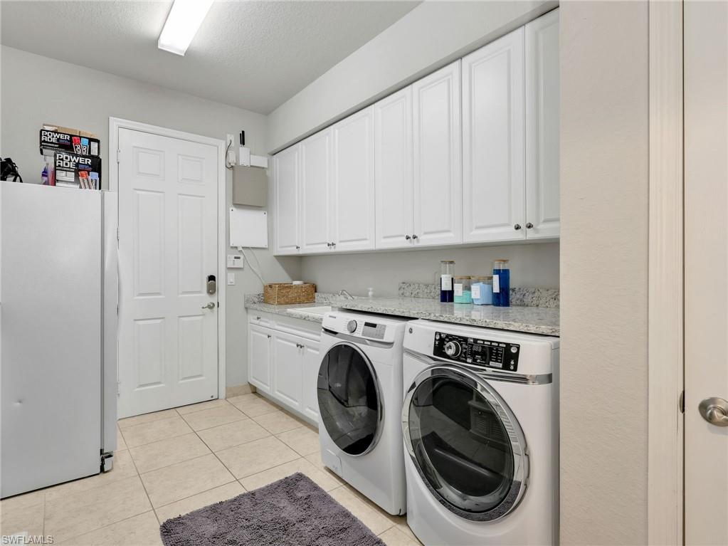 Utility room with tile flooring, extensive white cabinetry, and granite-look countertops