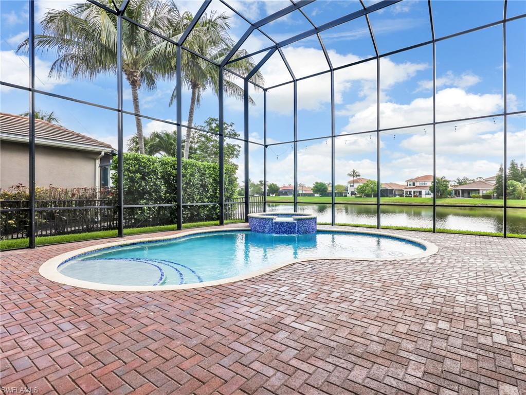 Screened lanai featuring a freeform swimming pool with integrated spa and brick paver decking
