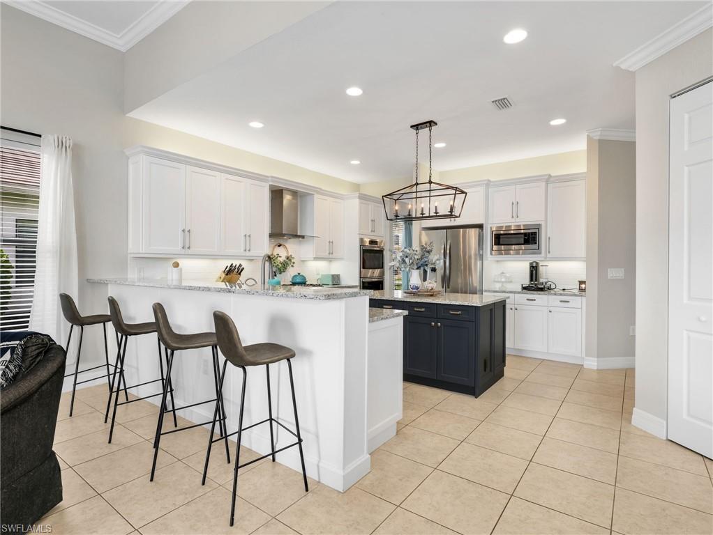 Open-concept kitchen featuring an oversized island, white shaker cabinetry, stainless steel appliances, and light-toned tile flooring