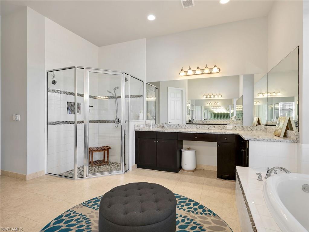 Spacious bathroom featuring a glass-enclosed shower with tile surround, a built-in soaking tub, extensive vanity with dual sinks and stone countertop, and large wall-mounted mirrors