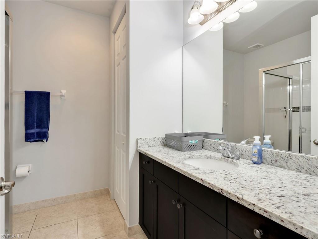 Spacious bathroom featuring a dark wood vanity with a white speckled countertop, an integrated sink, a large wall-mounted mirror, and a glass-enclosed shower