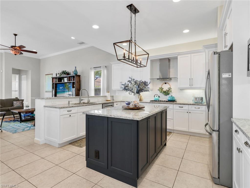 Spacious kitchen featuring a central island with a contrasting base, light-toned granite countertops, white cabinetry, stainless steel appliances, and tile flooring