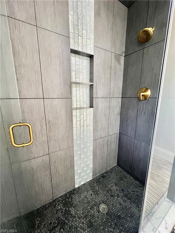 Walk-in shower featuring large format wall tiles, a mosaic tile accent strip, and a pebble-style floor