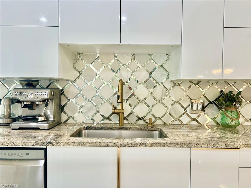 Kitchen featuring a geometric mosaic tile backsplash, white flat-panel cabinetry, granite countertops, and a gold-toned faucet