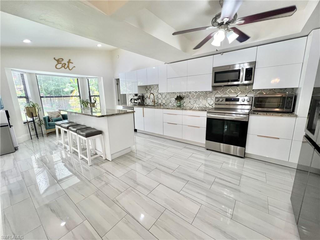 Modern kitchen featuring white cabinetry, stainless steel appliances, a center island with granite countertop, decorative backsplash, and wood-finish flooring