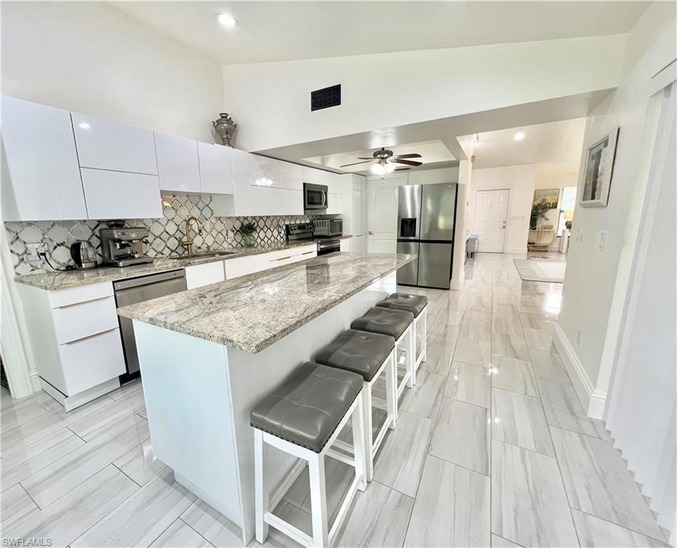 Contemporary kitchen featuring an expansive island with a granite countertop, stainless steel appliances, and sleek white cabinetry