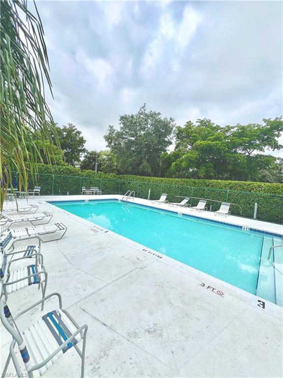 Rectangular community swimming pool featuring a tiled waterline, metal handrails, and a concrete deck