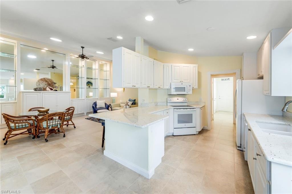 Spacious open-concept kitchen and living area featuring light-toned tile flooring, white cabinetry, integrated appliances, and light-colored countertops