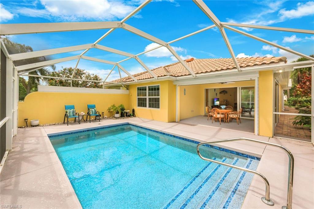 Screened-in pool area featuring a rectangular swimming pool with integrated steps and handrail, a spacious concrete paver deck, and a yellow stucco exterior