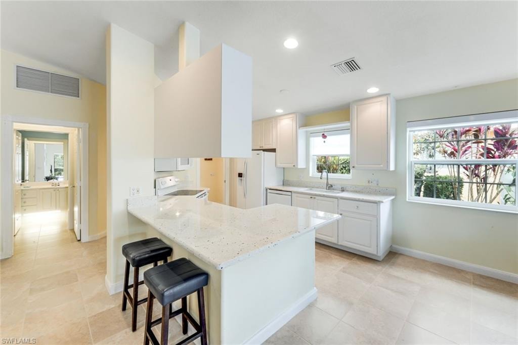 Open-concept kitchen featuring an island with a breakfast bar, white cabinetry, a built-in range, and a dual-basin sink under a window