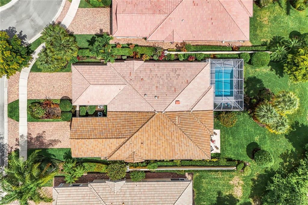 Tile roof residence featuring a screened pool enclosure, lush green landscaping, mature trees, and a paver driveway