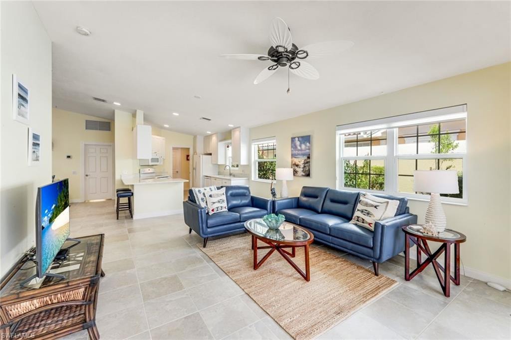 Spacious living area featuring high vaulted ceilings, large windows with white blinds, and light-toned tile flooring