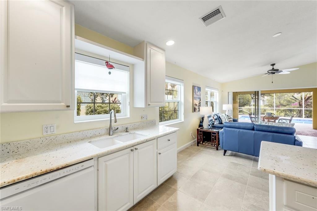 Kitchen sink area with light-toned countertops, white cabinetry, and a window overlooking exterior greenery
