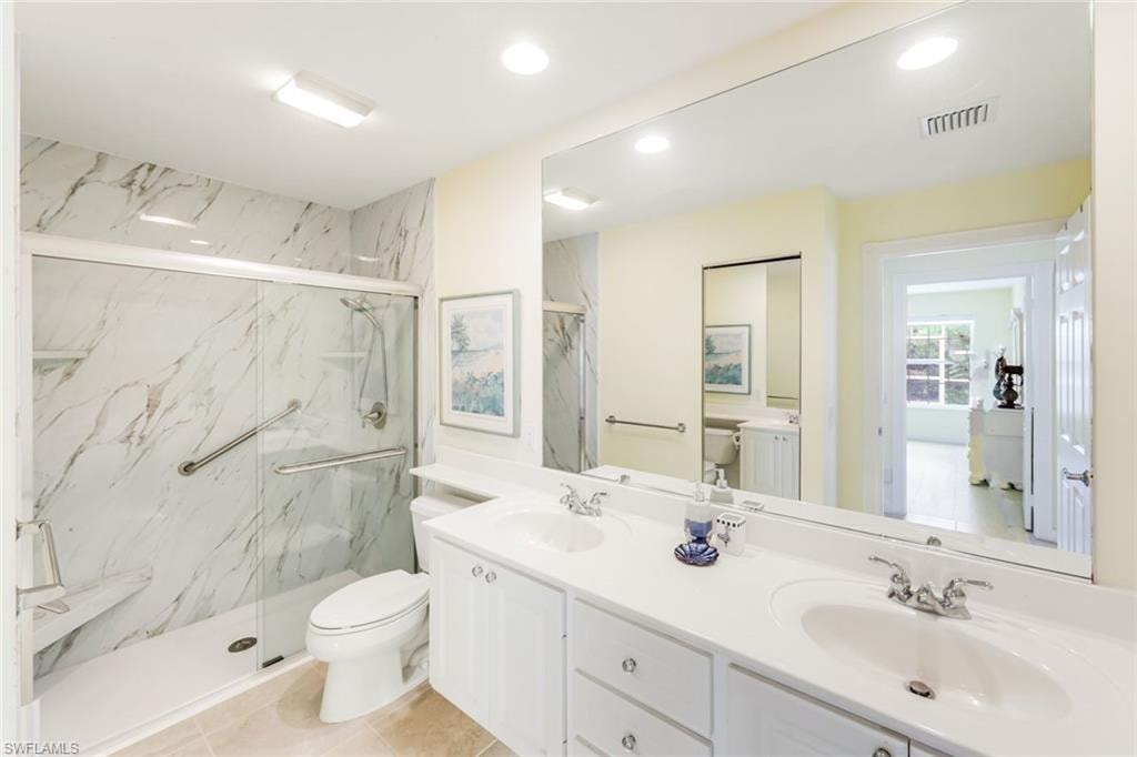 Bathroom featuring a dual vanity with white cabinetry, a spacious mirror, and a shower with sliding glass doors