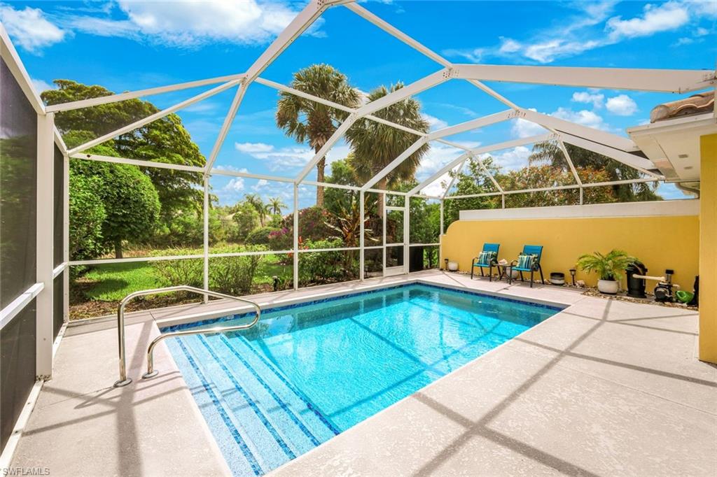 Screened outdoor pool area featuring a blue-tiled swimming pool with integrated steps, a surrounding concrete deck, and lush perimeter landscaping
