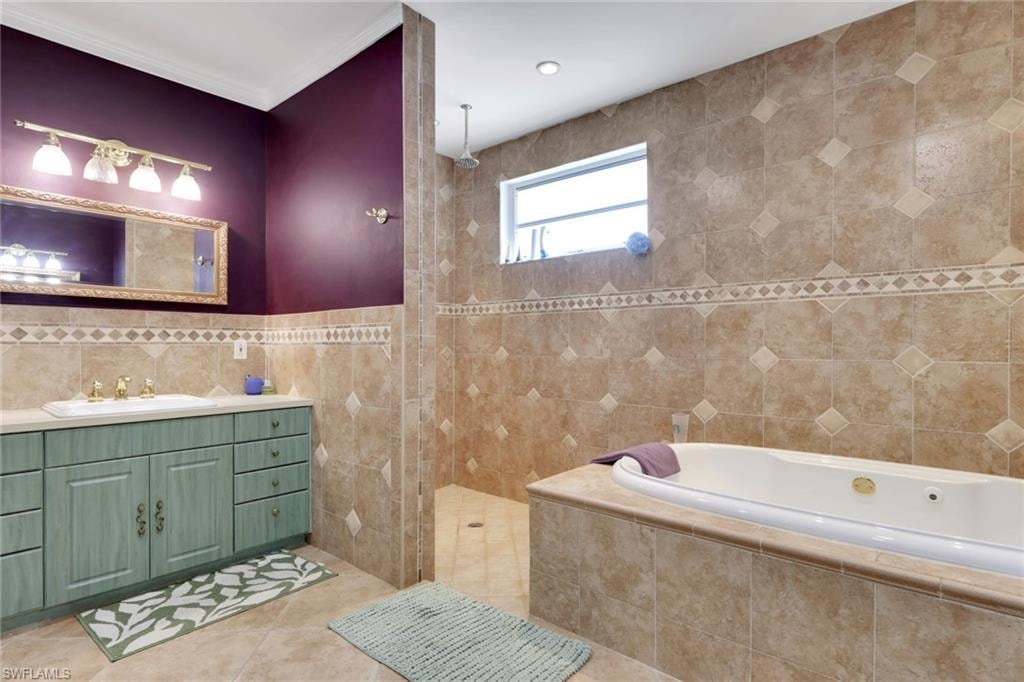 Bathroom featuring a jetted soaking tub, a separate tiled shower, a vanity with a built-in sink, and a framed mirror