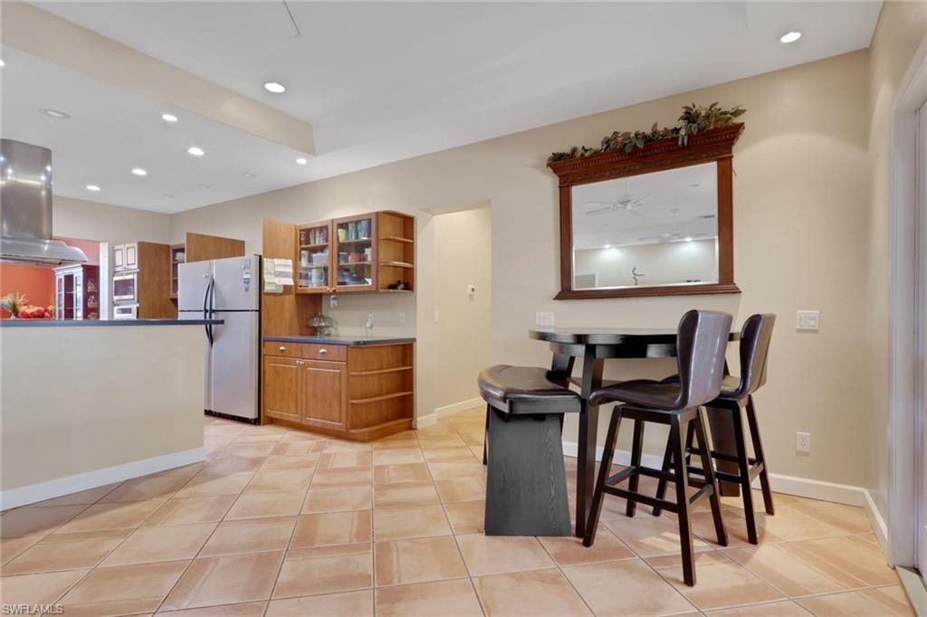 Expansive kitchen featuring tile flooring, recessed lighting, wood cabinetry with glass-front uppers, and stainless steel appliances
