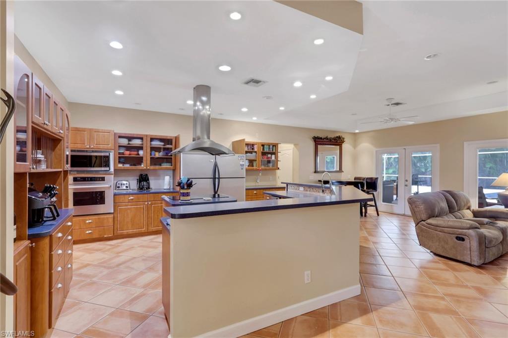 Spacious kitchen featuring warm wood cabinetry, stainless steel appliances, a central island with a breakfast bar, recessed lighting, and tile flooring