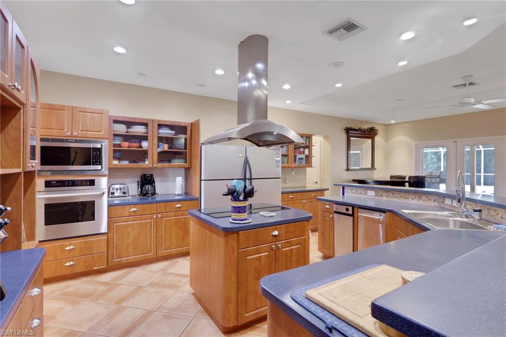 Spacious kitchen featuring wood cabinetry, blue countertops, stainless steel appliances, and an island with a built-in cooktop