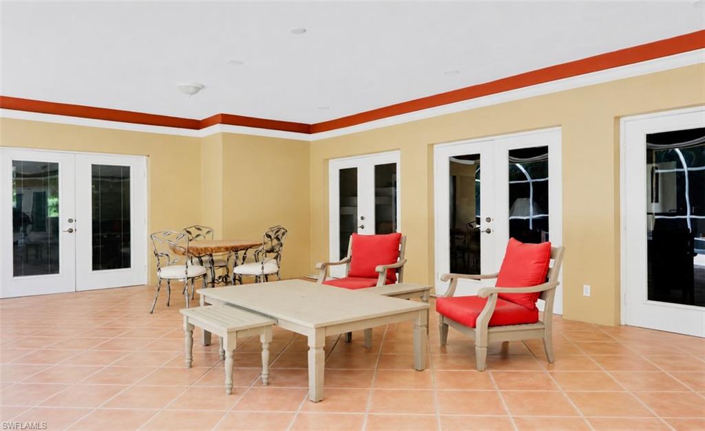 Spacious covered patio featuring large format tile flooring, multiple French doors, beige walls with red and white trim, and an overhead light fixture