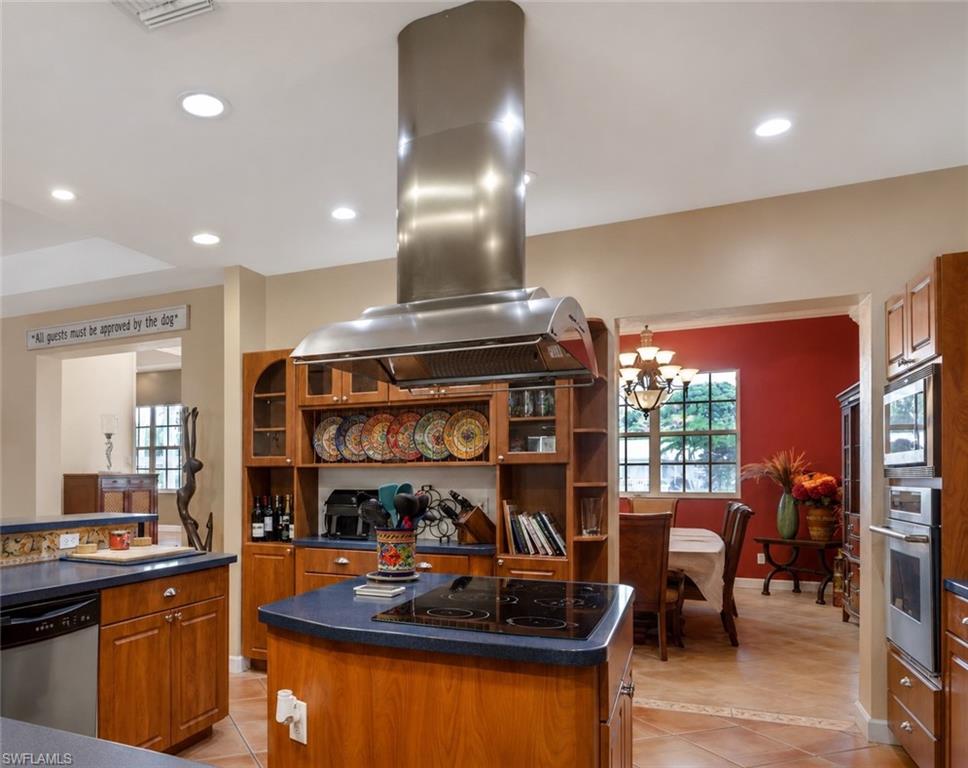 Kitchen featuring a stainless steel island range hood, built-in wall ovens, recessed lighting, wood cabinetry, and contrasting countertops