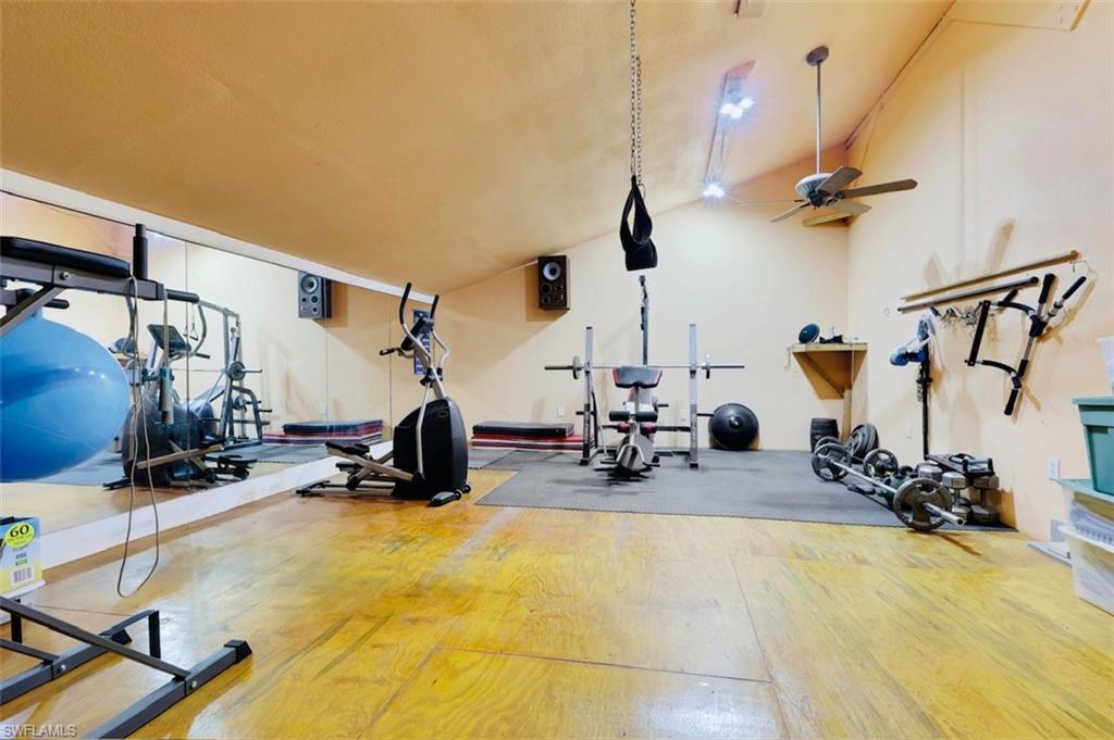 Spacious room featuring wood-finish flooring, a full-wall mirrored section, and a ceiling fan