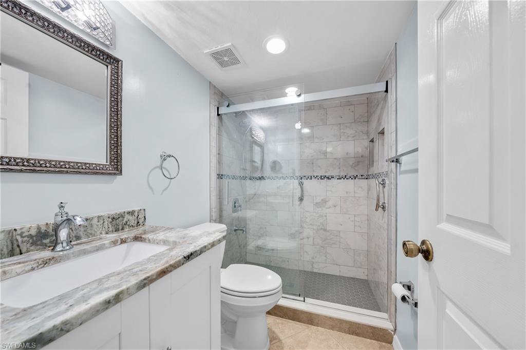 Bathroom featuring a white vanity with a marbled countertop, a framed mirror, and a glass-enclosed shower with tiled walls and flooring