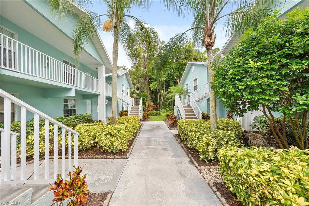 Landscaped pathway between two-story residential buildings featuring white railings and mature palm trees
