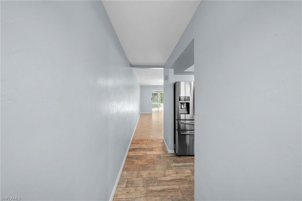 Hallway with tile flooring and a stainless steel refrigerator visible through an arched entryway