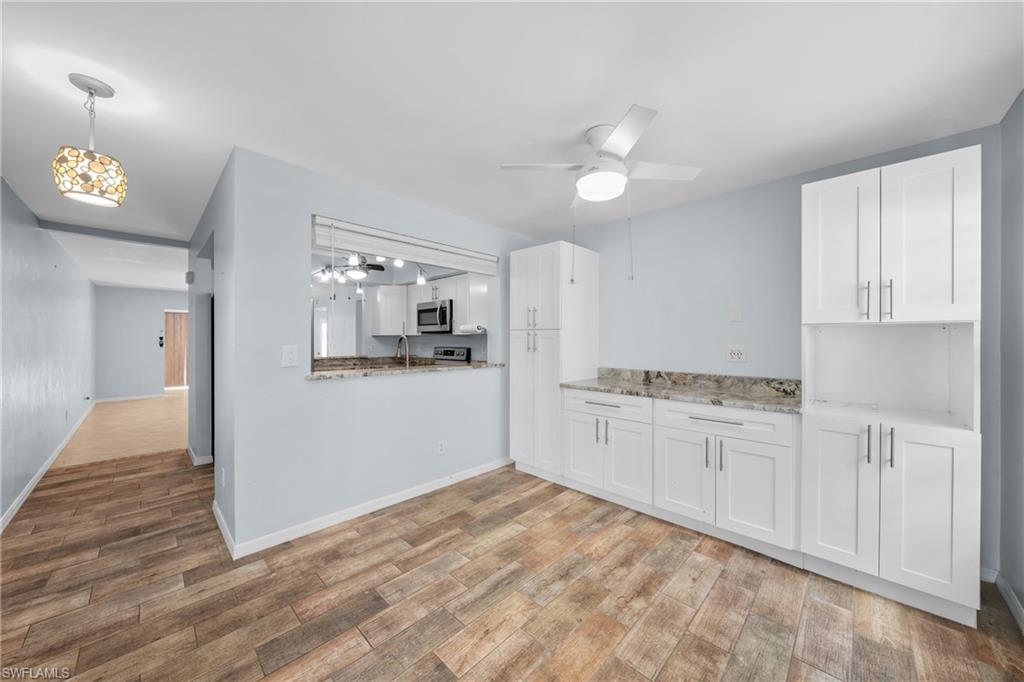 Dining area featuring wood-finish flooring, a ceiling fan with integrated lighting, and a pass-through window to the kitchen