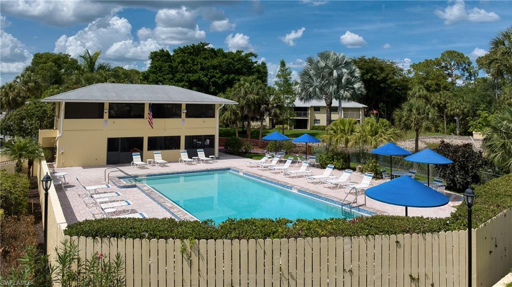 Community swimming pool featuring a spacious paver deck, perimeter landscaping, and a two-story clubhouse with screened balconies