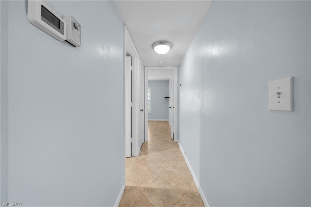 Hallway featuring light blue walls, tan tile flooring, white trim, and a contemporary ceiling light fixture