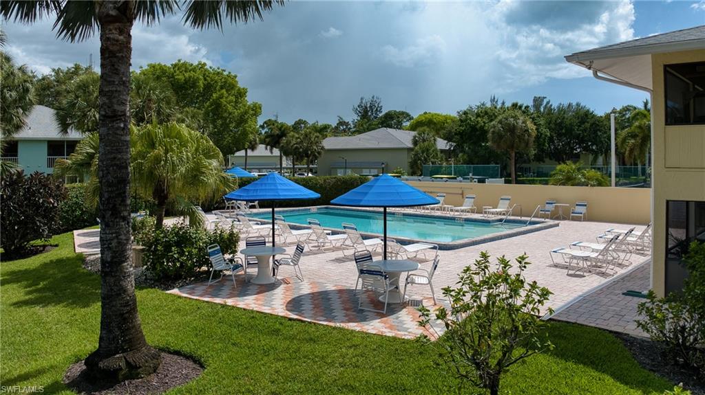 Community swimming pool with a surrounding paver deck, umbrella-shaded tables, and dedicated lounge areas