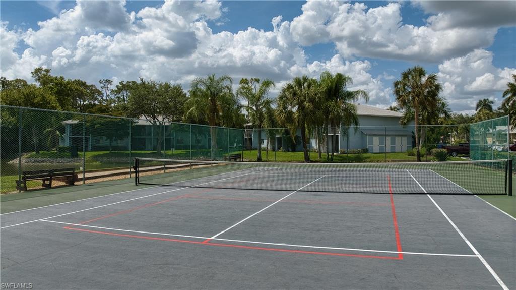 Hard surface tennis court featuring a net and perimeter fencing