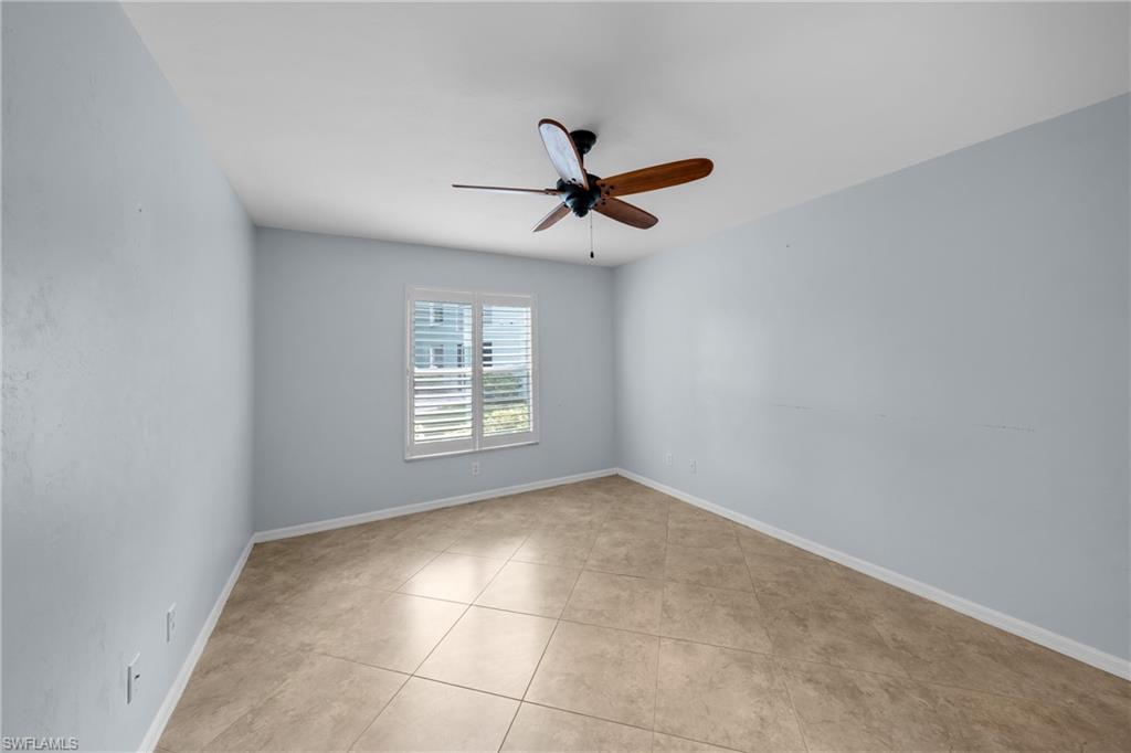 Interior room featuring a single window with white plantation shutters, a ceiling fan with wood-tone blades, and diagonal tile flooring